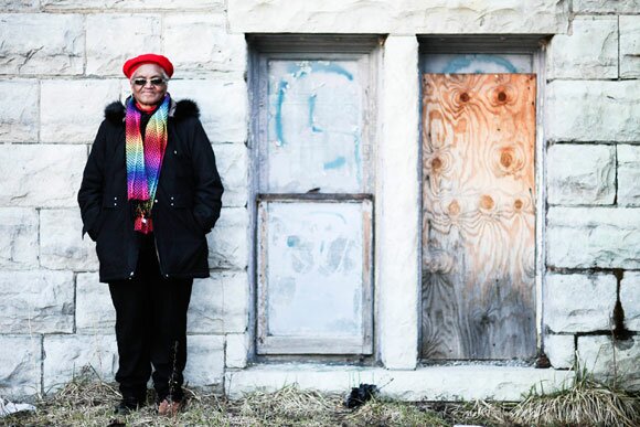 Alice Davis, in a red hat and rainbow scarf, stands before boarded windows outside St. Matthew's