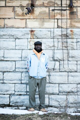 Frank Beard, in a beret and light blue jacket, standing against an exterior wall of St. Matthew's