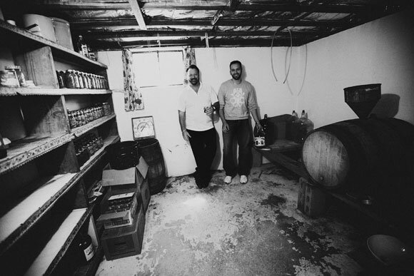 two Caucasian men, standing in the back of a room with wine barrels