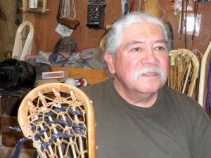 upper body of a man with white hair and a white mustache holding a wooden lacrosse stick