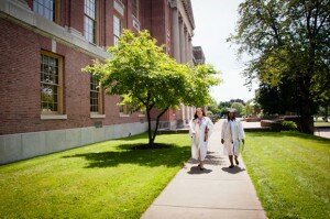 Two young women in graduation robes walking down a path in front of a high school